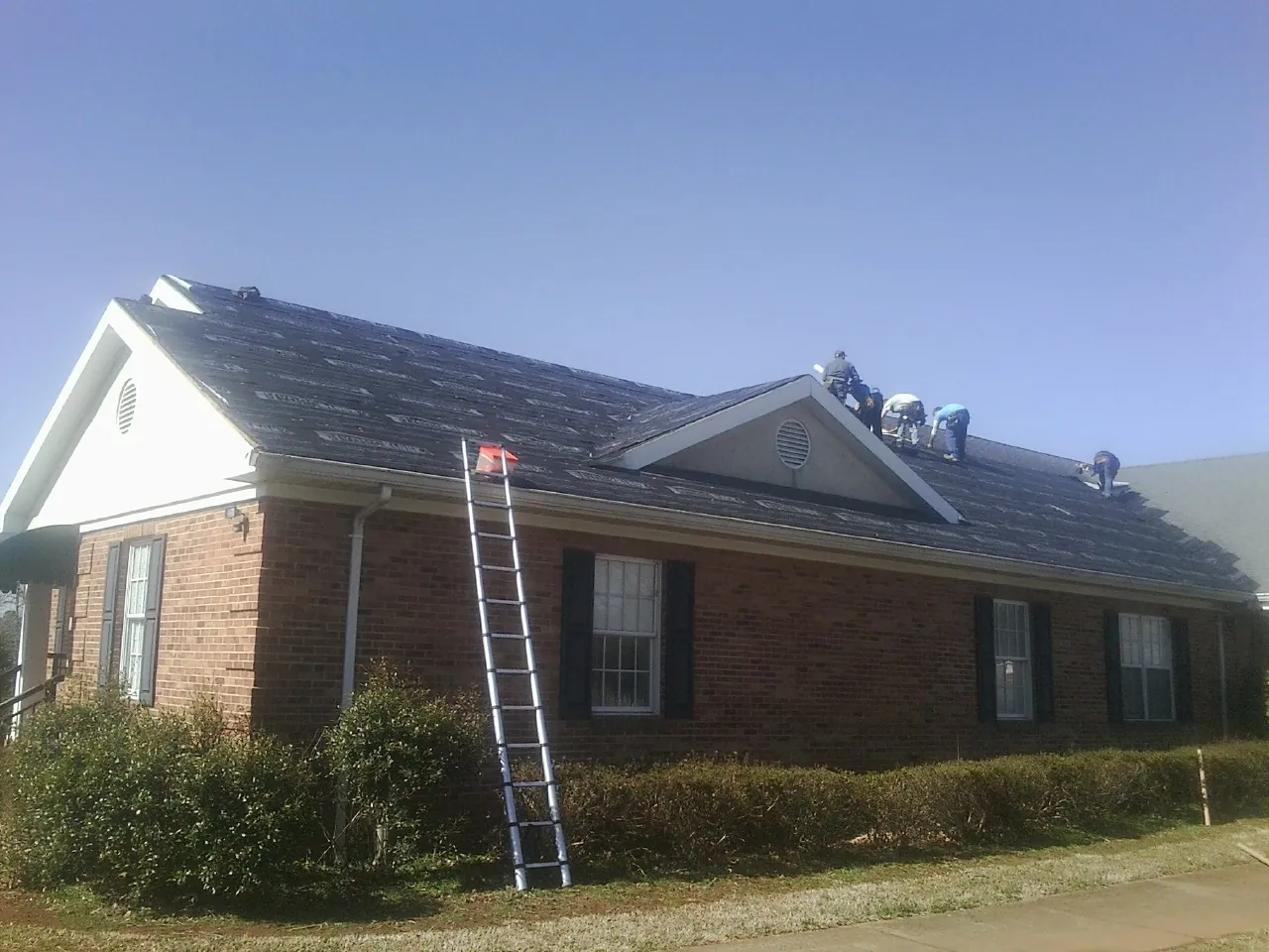 Crew tearing shingles off a brick ranch roof with a ladder set — Emergency Roof Repair work by our crew in Lyle