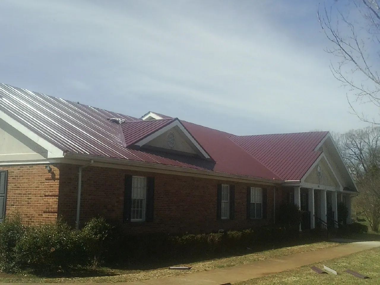 Red metal roof with gabled entries on a long brick building, from a Hail Damage Roof Repair job in Lyle